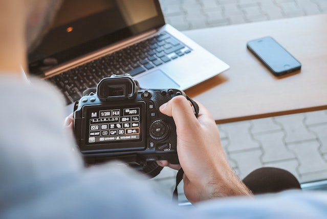 an over the shoulder view of a landlord holding a digital camera prior to uploading photos of their vacant property to their laptop